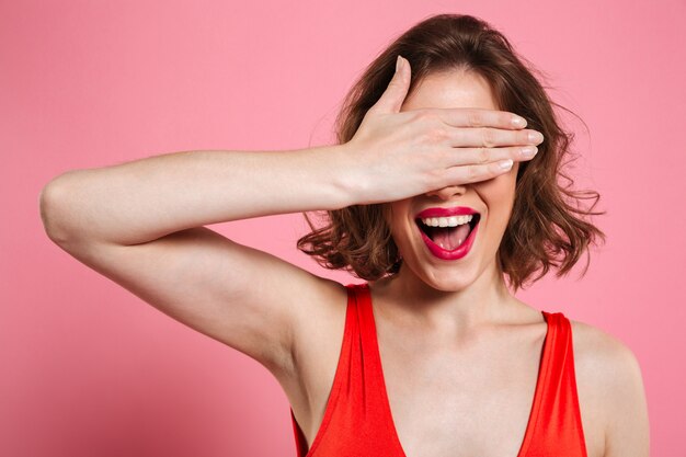 Close-up portrait of charming smiling brunette woman hiding eyes under hand