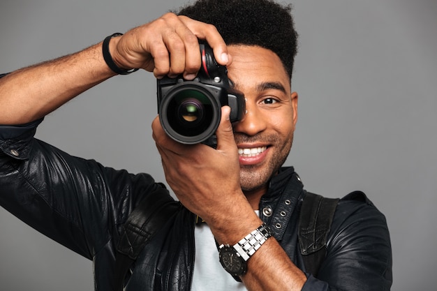 Close-up portrait of cheerful african man looking through cameras objective while taking photo