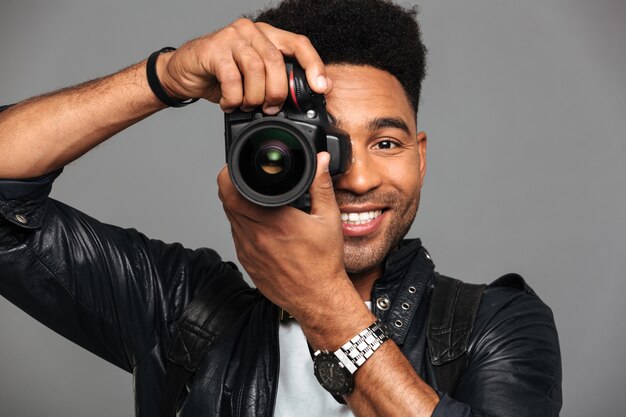 Close-up portrait of cheerful african man looking through cameras objective while taking photo