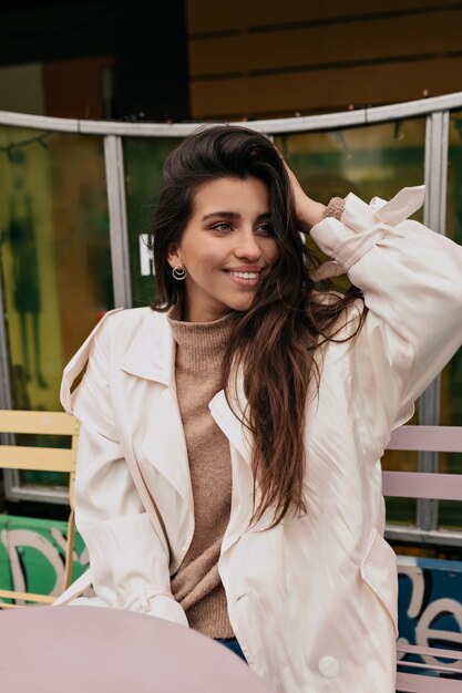 Close-up portrait of cheerful woman in white coat her hair on open air terrace