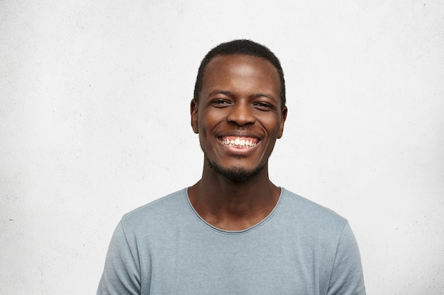 Free photo close up portrait of cheerful young black man in grey t-shirt smiling broadly