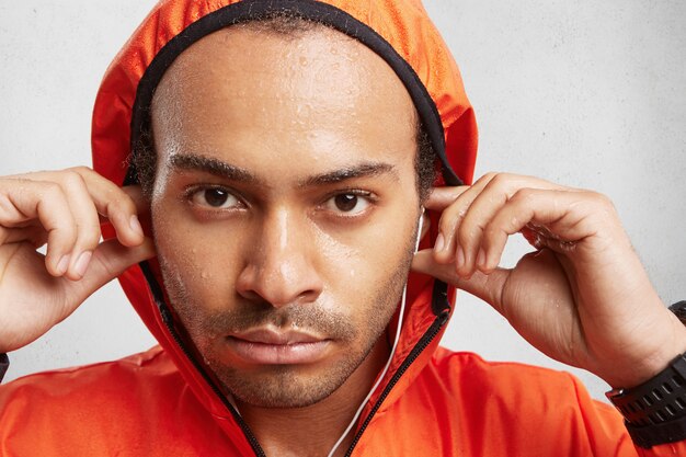 Close up portrait of confident dark skinned male with bristlle, wears hood from anorak