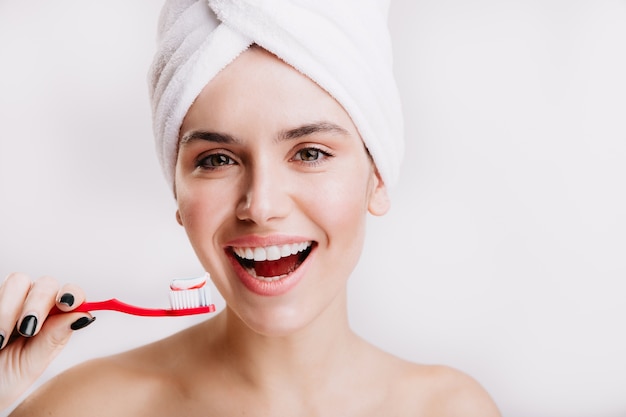 Close-up portrait of contented girl with towel on her head. Brunette with snow-white smile is holding toothbrush.