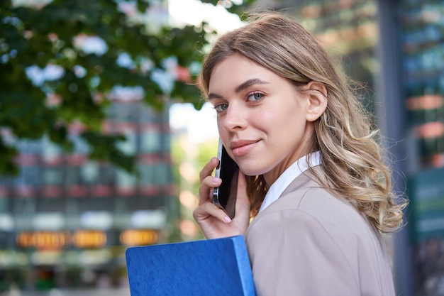 Close up portrait of corporate woman calling on mobile phone walking on street with work documents i