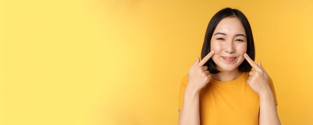 Close up portrait of cute asian girl showing her dimples and smiling coquettish at camera standing o