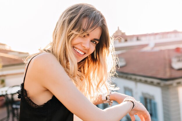 Close-up portrait of cute blonde girl with charming smile standing on observation deck in morning