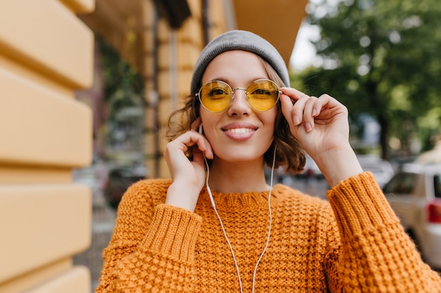 Close-up portrait of cute european lady with nude make-up listening music while walking down the street in autumn day