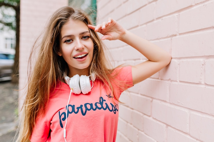 Free Photo close-up portrait of cute girl with long hair and beautiful smile standing beside wall