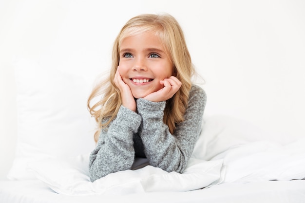 Close-up portrait of cute little girl holding her head, looking asode while lying in bed