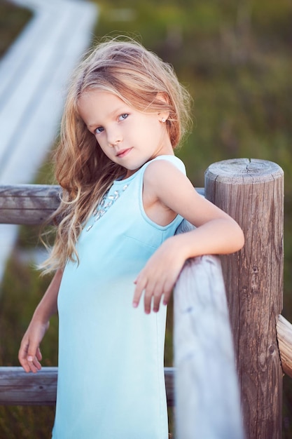 Close-up portrait of a cute little girl, standing outdoors while leaning on a wooden fence.