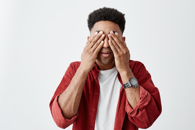 Крупным планом портрет темнокожих мужчин одежда глаза руками, пытаясь расслабиться после долгого времени работы с ноутбуком в офисе. Парень с головной болью и усталостью.