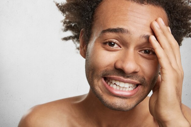 Close up portrait of dark skinned stubble man being naked, keeps hand on head,