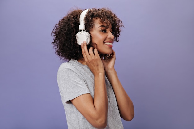 Close-up portrait of dark-skinned woman in headphones on purple wall