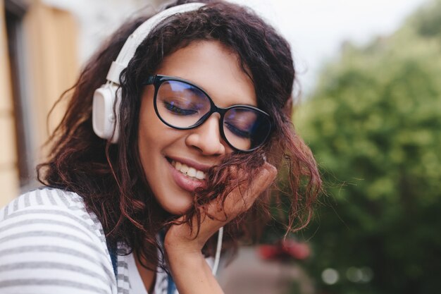 好きな歌を楽しんでいる薄茶色の肌を持つ夢のような若い女性のクローズアップの肖像画