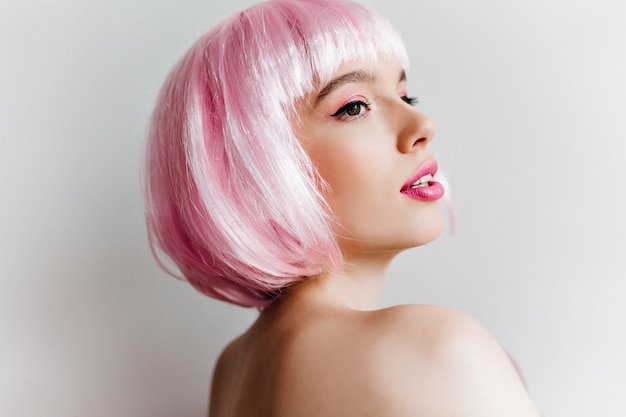 Close-up portrait of elegant young woman in pink wig looking away with interest. Amazing caucasian girl with short straight hair posing on light wall.