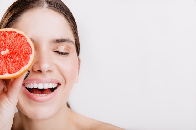 Close-up portrait of energetic laughing girl without makeup covering her face with Sicilian orange.