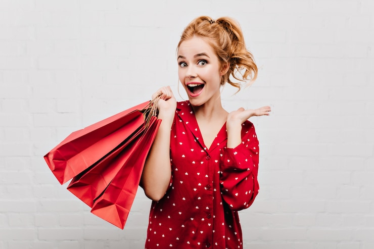 Free Photo close-up portrait of excited woman with wavy hairstyle holding red paper bag. emotional girl in night-suit having fun on white wall