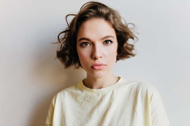 Close-up portrait of fascinating serious girl isolated on white wall. Spectacular european female model with curly hairstyle