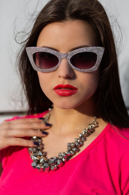 Close up portrait of fashionable brunette woman in stylish sunglasses and pink t-shirt.