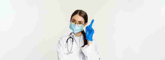 Free photo close up portrait of female doctor in glasses medical face mask and gloves pointing finger up at lin