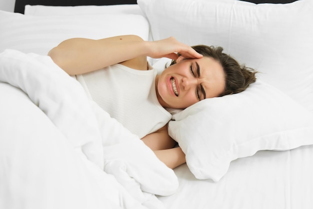 Free photo close up portrait of female model lying in bed with headache grimacing and frowning from painful