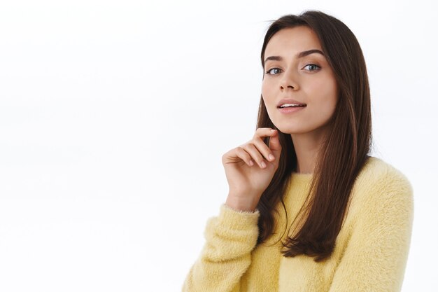 Close-up portrait feminine good-looking young confident woman with perfect skin, no blemishes, natural look, gazing camera curious and sassy, white wall