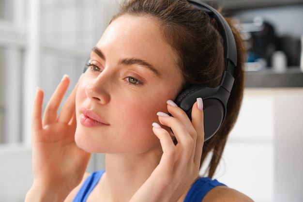 Close up portrait of fitness woman smiling and listening music wearing wireless black headphones