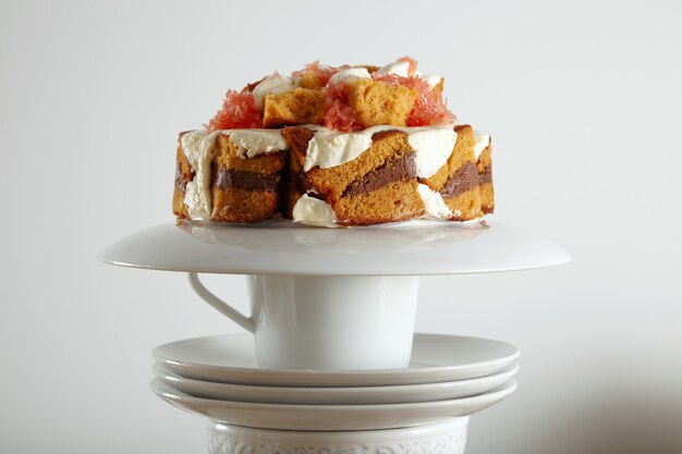 Close up portrait of a fresh sweet brown sponge cake with chocolate, cream and grapefruit on white cups and saucers isolated on white