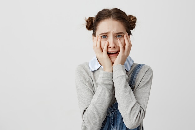 Close up portrait of frightened woman in denim covering her face with hands being shocked. Young female screaming in panic being in trouble can't believe in truth. Emotions concept