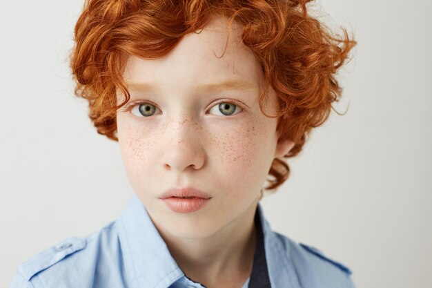 Close up portrait of funny little kid with orange hair and freckles. Boy looking with relaxed and calm face expression.