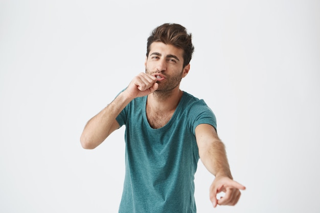 Close up portrait of funny unshaved handsome caucasian guy in trendy clothes and good hairstyle, fooling and singing while nobody seeing him. Body language
