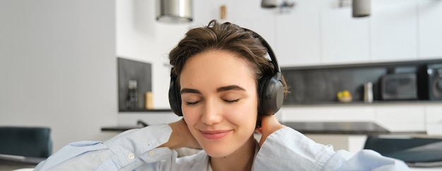 Free photo close up portrait of girl with headphones enjoys listen to music close eyes and smiles form joy and