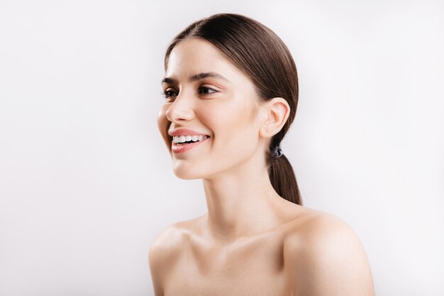 Close-up portrait of girl with perfect clear skin and shiny healthy hair, posing with snow-white smile on isolated wall.