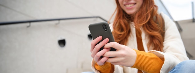 Foto gratuita ritratto ravvicinato delle mani delle ragazze che tengono lo smartphone. la donna si siede sulle scale sulla strada e usa il cellulare