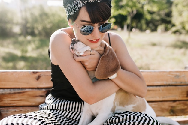 Close-up portrait of glad brunette lady embracing her beagle dog with gently smile.