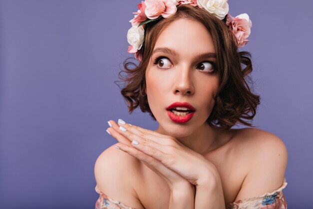 Close-up portrait of good-looking dreamy woman with roses in hair. Indoor photo of wonderful girl in wreath standing.