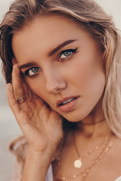 Close up portrait of gorgeous blond woman with perfect skin and blue eyes posing on the beach