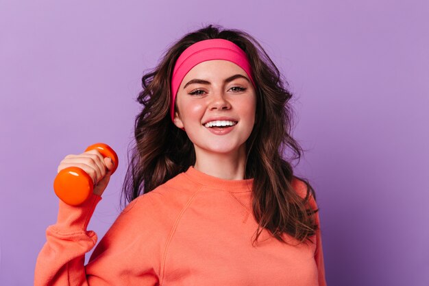 Close-up portrait of green-eyed curly woman in orange sweater and pink sports headband