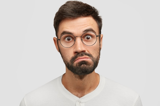 Close up portrait of handsome angry surprised man looks in bewilderment, purses lips and stares