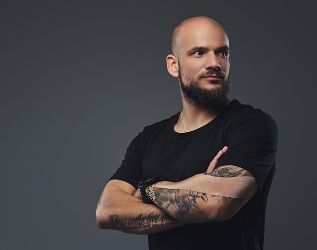 Close-up portrait of a handsome bearded athlete in a black t-shirt, posing with crossed arms in a studio. Isolated on a gray background.