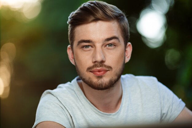 Close up portrait of handsome confident young man in white t-shirt on blurry outdoor nature