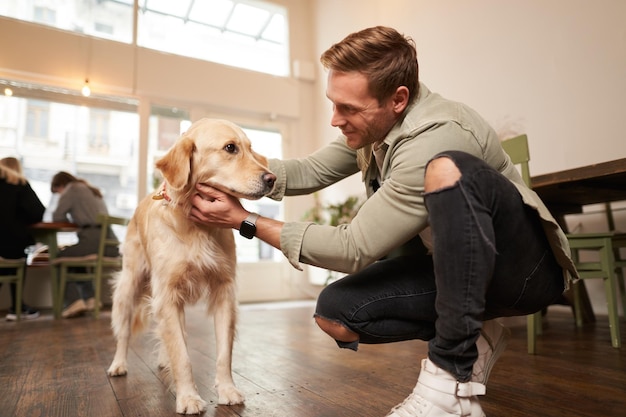 ペットフレンドリーなカフェのコーヒーショップで可愛い犬を撫でているハンサムな幸せな男のクローズアップ肖像画