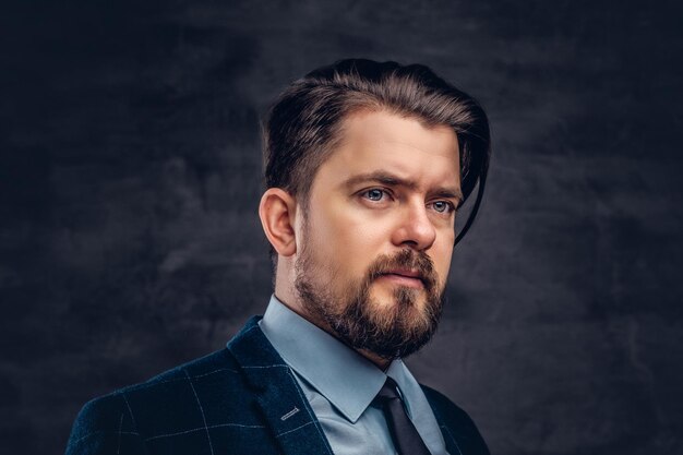 Close-up portrait of a handsome middle-aged man with beard and hairstyle dressed in an elegant formal suit on a textured dark background in studio.