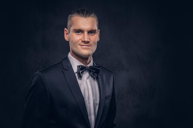 Close-up, a portrait of a handsome stylish man in an elegant black suit over a dark background.