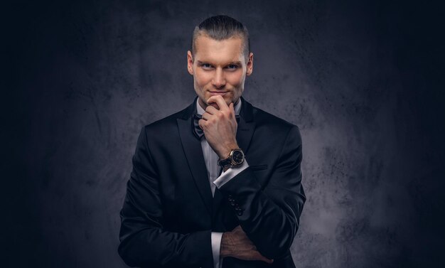 Close-up, a portrait of a handsome stylish man in an elegant black suit over a dark background.