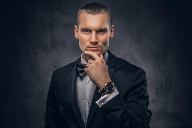 Close-up, a portrait of a handsome stylish man in an elegant black suit over a dark background.