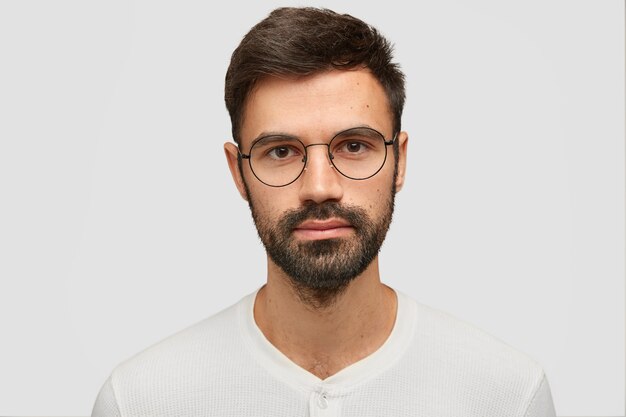 Close up portrait of handsome unshaven man with thick beard and mustache, has dark hair, looks seriously