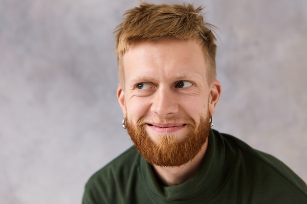 Free photo close up portrait of handsome young caucasian male with stylish hairdo and trimmed beard posing isolated looking away with mysterious smile, feeling highly flattered. positive human expressions