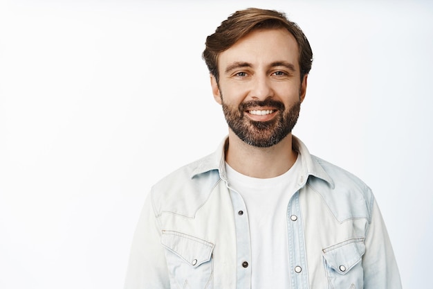 Foto gratuita close up ritratto di felice uomo barbuto con un sorriso bianco in piedi in abiti casual su sfondo bianco