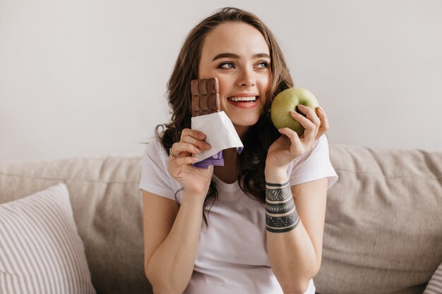 Close-up portrait of happy brunette young woman holding green apple and sweet milk chocolate